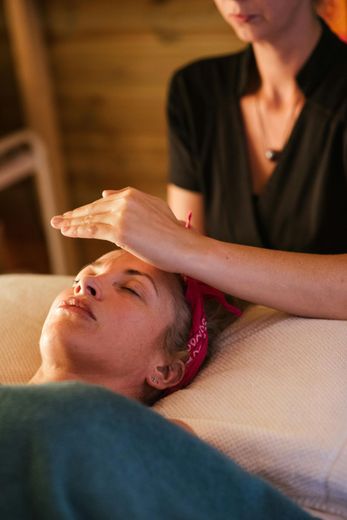 Spa therapist giving a facial massage to a reclining client in a warm, dimly lit room